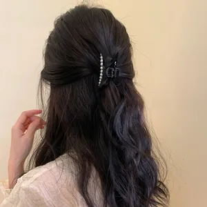 Detail of a black silk bow hair claw with white pearls styled on wavy brunette hair