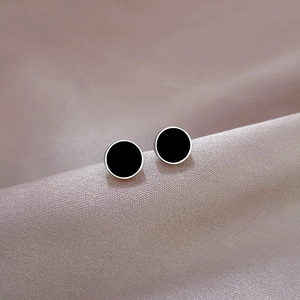 Macro shot of minimalist black round stud earrings on purple silk fabric background