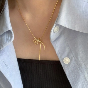 Close-up of golden bow-knot pendant necklace worn by a model against blue shirt
