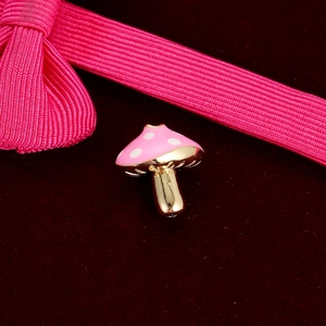 Macro shot of a pink and white mushroom enamel charm on dark red velvet with ribbon