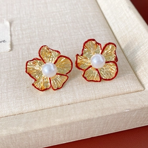 Detail eines roten Blumenohrrings mit Goldbasis und einer weißen Perle in der Mitte