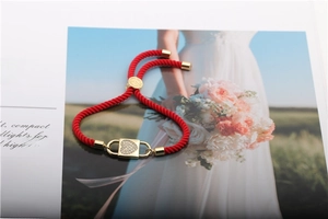 Detail of red cord bracelet with a heart-shaped gold charm and micro-set cubic zirconia