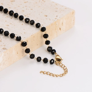 Minimalist black beaded necklace with gold infinity charm on natural stone background