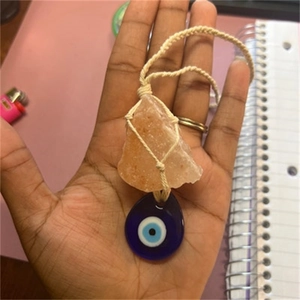 Detail of evil eye charm and raw pink crystal pendant on a handmade braided necklace