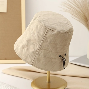 Minimalist beige quilted bucket hat with adjustable cord shown on a metal display stand