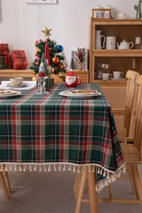 Detailed view of red plaid Christmas tablecloth with beige tassels on a wooden table