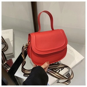 Detail of red PU leather saddle bag with removable red and green striped wide strap