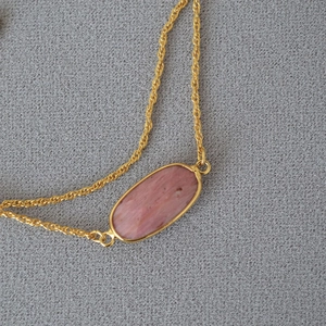 Elegante collana a catena dorata con pendente ovale in pietra naturale rosa su tessuto grigio
