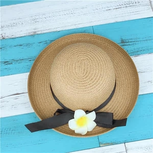 Detailed top view of wide brim straw sun hat with black ribbon and plumeria flower