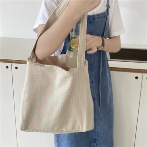 Detalle de un bolso tote de lona a cuadros rosa y verde sostenido por una modelo informal