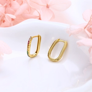 Macro detail of U-shaped gold earrings featuring multi-color stones on white ceramic