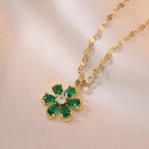 Close-up of golden heart flower pendant with green gemstones on soft pink silk