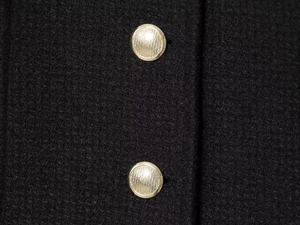 Detailed close-up of black tweed fabric with premium gold textured buttons on the jacket