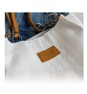Close-up of white quilted tote bag with brown leather tag and silver metal ring hardware