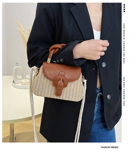 Detail of straw flap bag featuring brown leather trim and white rope shoulder strap