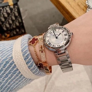 Elegant ladies watch with roman numerals layered with clover bracelet and gold bangle