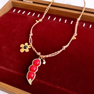 Macro shot of pea pod pendant with red stones and gold flower on velvet tray
