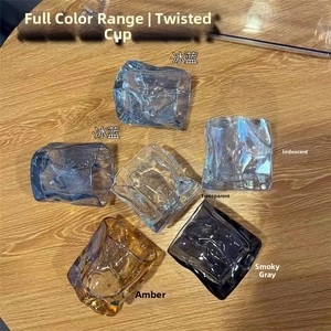 Detail showing irregular twisted glass tumblers in blue, clear, and amber on wood surface