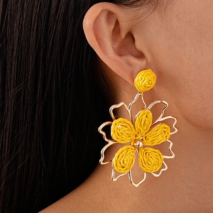Detalle de pendientes de flores de rafia amarilla con bordes dorados en la modelo