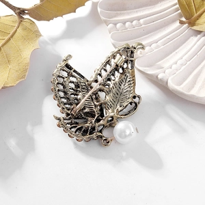 Vintage metal butterfly brooch with rhinestones and pearl pendant shown on white surface