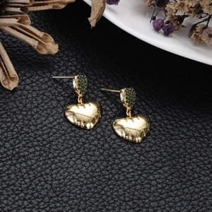 Detail of gold heart earrings with green zircon accents on black leather texture