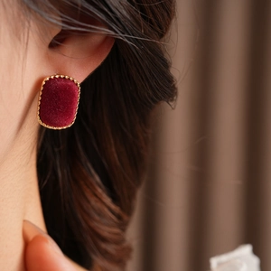 Close-up of a burgundy velvet square stud earring with a golden woven metal edge on model