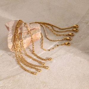 Detail of gold-plated chains with cubic zirconia accents on a stone background