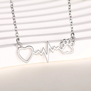 Silver heartbeat necklace with hollow cat paw and heart pendant on white stand