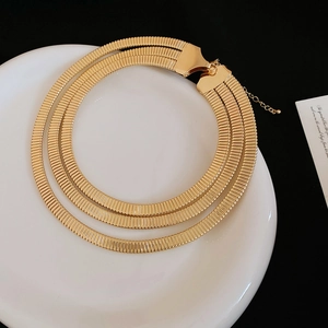 Detail showing triple-layered gold snake chain necklaces on a white ceramic plate