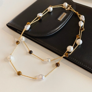 Detail of tiger eye beads and baroque pearls on a gold chain over a black leather clutch