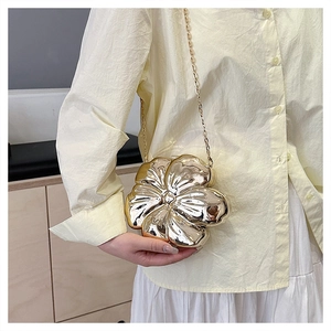 Detail of a metallic gold flower-shaped chain bag with a polished mirror finish surface