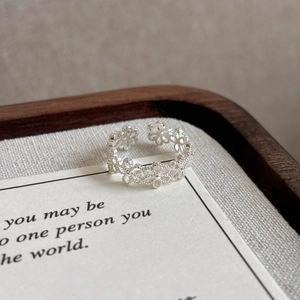 Minimalist silver open ring with hollow flower design on a textured fabric background