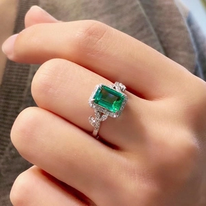Detail of emerald cut green gemstone ring with leaf accents and halo setting on finger