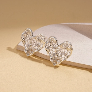 Macro view of silver heart stud earrings with a hollow mesh texture on a modern prop