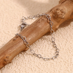 Detail of silver heart-shaped link chain with lobster clasp on a rustic wooden branch