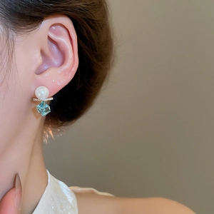 Detail showing 18k gold earrings with blue square gemstone and white pearl on model