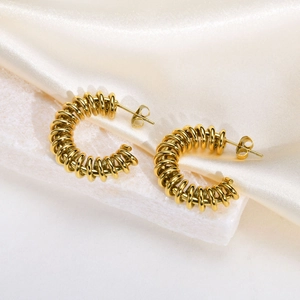 Golden spiral twisted C-shape earrings on white stone base with soft cream silk background