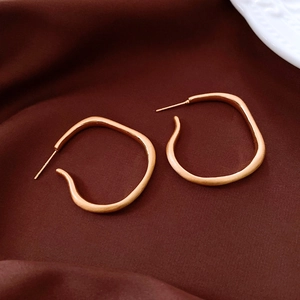 Macro shot of gold-plated irregular geometric earrings on dark velvet background