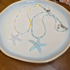Detail of beaded necklaces with iridescent resin starfish pendants on ceramic plate