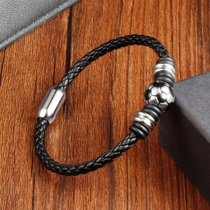Detail of black woven leather bracelet with metal football bead on wooden surface