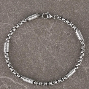 Silver stainless steel box chain bracelet with cylindrical beads on stone surface