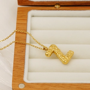 Macro shot of gold letter L pendant with lava texture on a wooden jewelry box