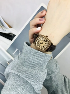 Detail of a square gold watch with diamonds and brown leather strap on a wrist