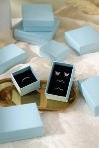 Flat lay of light blue jewelry boxes with black lining holding a butterfly stud and ring