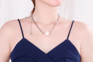 Detail of asymmetric chain necklace featuring a white pearl and metallic ball tassel pendant