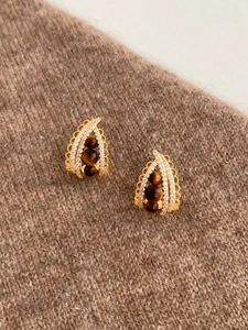 Detail view of gold earrings with tiger eye stones and zircon pave on soft knit fabric