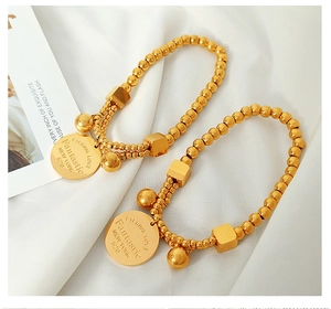 Detail of 18k gold beads bracelet featuring square charms, bells and engraved coin tags