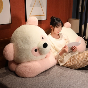 Coussin panda en peluche rose et beige présenté dans une chambre à coucher chaleureuse