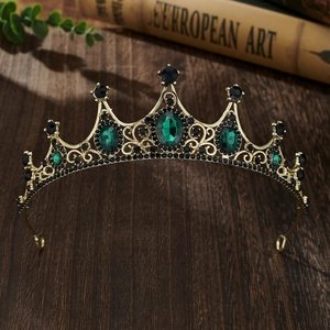 Close-up of vintage golden crown with emerald green gems on dark wooden background