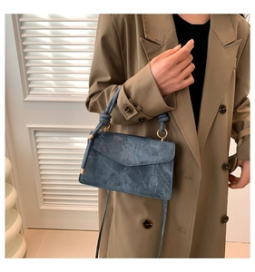 Détail du mini sac bleu texturé avec poignée nouée et bandoulière dotée d'anneaux métalliques